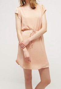 Vestido de color durazno hecho de tela ligera, con mangas cortas, escote redondo y detalle de lazo en la cintura. Textura suave, ajuste relajado.