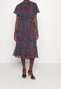 Klänning med paisleymönster, korta fladdrande ärmar, krage och flödande kjol. Flerfärgad i gröna, röda och blå toner.