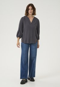 Donkergrijze textuur blouse met een V-hals en gathered ballonmouwen, gecombineerd met een wijde spijkerbroek en zwarte plateau schoenen.