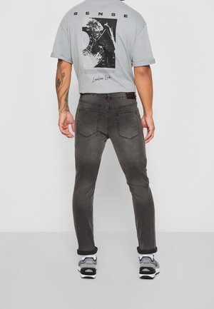Grå t-shirt med grafiskt tryck på ryggen, kombinerad med slim-fit, blekta svarta jeans och sneakers. Har uppvikta ärmslut och minimalistiska detaljer.