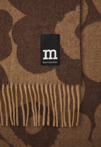 Wool blanket featuring a brown and beige floral pattern with fringe edges. Includes a black tag with white lettering from Marimekko.