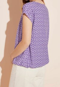 Top viola a maniche corte con un motivo geometrico di ovali sovrapposti, caratterizzato da una vestibilità rilassata e una consistenza della trama liscia.