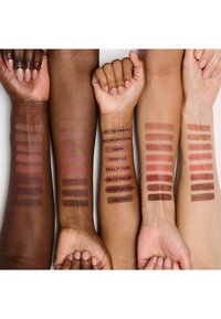 Quatre bras présentent des échantillons de différentes couleurs de rouge à lèvres sur diverses teintes de peau, étiquetés avec des noms tels que « Off the Market » et « Chestnut ».