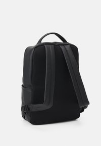 Sac à dos noir au design élégant, doté d'un dos en mesh texturé, de bretelles rembourrées et d'une poignée supérieure pour plus de commodité lors du transport.