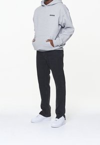Grå huva sweatshirt med svart logotyp, känguruficka, kombinerat med svarta jeans och vita sneakers. Enkelt, avslappnat outfit.