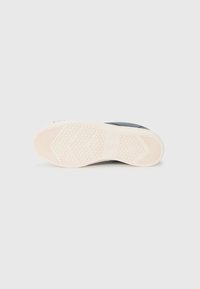 Shoe sole in rubber, featuring a textured, white bottom with hexagonal and striped patterns, and a dark colored upper part visible at the edges.