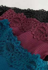 Lace-trimmed tops in teal, burgundy, and black. De stof heeft een geribbelde textuur en de kant heeft bloemmotieven langs de randen.