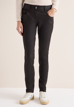 Czarne jeansy slim-fit z przednimi kieszeniami, dopasowany krój i gładka tekstura. W połączeniu z białymi trampkami z niebieskimi akcentami.
