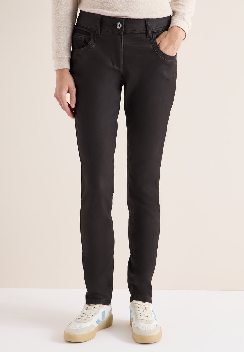 Svarta slim-fit jeans med framfickor, åtsittande design och slät textur. Matchat med vita sneakers med blå accenter.