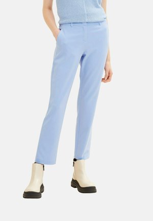 Pantalons ajustés bleu clair, avec une coupe slim, présentant une texture lisse et des passants de ceinture, associés à des bottines crème et un haut texturé.
