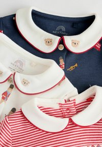 Drei Baby-Polohemden: navy mit Bärenmotiven und weißem Kragen, creme mit Bärenakzenten und rotem Saum sowie rotgestreift mit weißem Kragen.