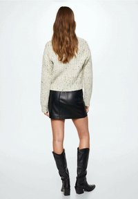 Strukturierter cremiger Pullover, figurbetonte schwarze Leder-Minirock und kniehohe schwarze Lederstiefel. Insgesamt lässiges, geschichtetes Outfit.