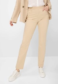 Beige trousers with a stretchy waistband, slim fit, and front pockets, paired with a light blazer and white sneakers. Smooth fabric.