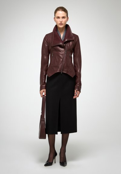 Veste en cuir bordeaux avec grand col, poches zippées, associée à une jupe noire et un sac à main assorti, créant une silhouette structurée.
