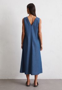 Denim maxi-kjole med V-rygg og brede stropper. Ensfarget blå, avslappet passform, jevn tekstur og ankel-lengde hem.