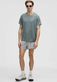 Grå kortærmet sportst-shirt med tekstureret overflade, kombineret med lysegrå shorts. Modellen bærer hvide solbriller og lyse sko.