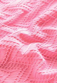 Tissu texturé rose présentant un motif en relief avec des lignes ondulées et des détails géométriques, affichant une apparence douce et lisse.