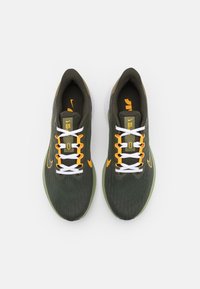 Baskets de course vertes avec une partie supérieure texturée, accents blancs et orange, lacets plats blancs et semelle en caoutchouc solide. Logo Nike sur les côtés.