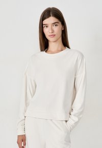 Felpa beige chiaro realizzata in tessuto morbido. Caratterizzata da un collo a giro e maniche scese. Design semplice e senza cuciture con una vestibilità rilassata.