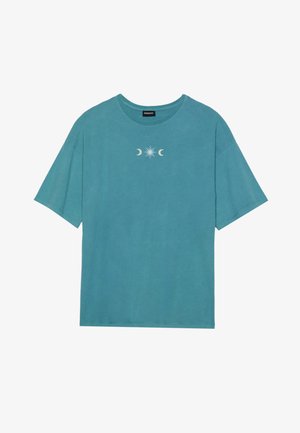 Teal bomulls T-skjorte, kort erm, rund hals, med et sentralt grafisk motiv av en stjerne og halvmåner i hvitt. Myk, uformell design.