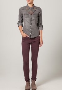 Camicia grigia con bottoni e due tasche sul petto, caratterizzata da un colorato colletto di perline. Abbinata a jeans skinny bordeaux e stivaletti beige.