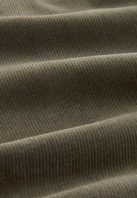 Gros plan d’un tissu doux et côtelé vert olive avec des plis légers et des lignes de texture verticales visibles.