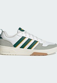 Basket basse en cuir blanc, avec des bandes vertes et jaunes, des accents en daim gris, des lacets blancs et une semelle en caoutchouc beige avec le logo Adidas.