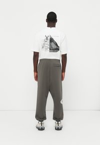 Hvid T-shirt med grafiske tryk på ryggen, parret med løstsiddende grå joggingbukser og grå sneakers med teksturerede såler.