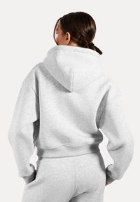 Hoodie grigio corto realizzato in morbido misto cotone. Presenta un ampio cappuccio e polsini a costine, con una vestibilità rilassata che mette in evidenza il comfort.