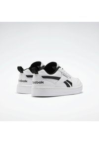 Baskets en cuir blanc avec des accents et un logo noirs. Elles présentent une semelle plate, un bout rond, et un logo contrastant à l'arrière.