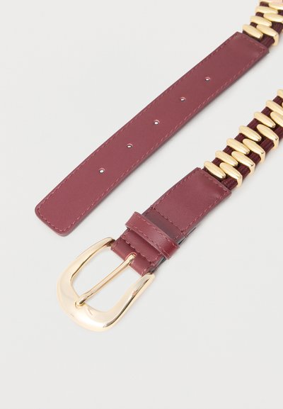 Ζώνη από βουργουνδί δέρμα με αγκράφα σε χρυσό τόνο και διακοσμητικούς χρυσούς κρίκους κατά μήκος της μίας πλευράς σε λευκό φόντο.