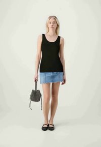 Top negru fără mâneci, fustă mini din denim cu margine desfăcută, balerini negri cu bătăi și o geantă mică cu model. Fundal neutru.