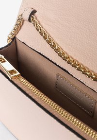 Interno di una borsa in pelle rosa pallido con tracolla in catena dorata, tasca con zip e hardware dorato, e etichetta del marchio cucita all'interno.