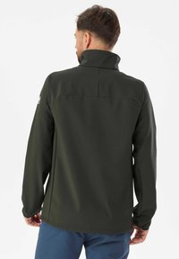 Veste softshell vert foncé avec un col montant, des manches longues et une texture lisse. Présente un détail de couture dans le dos et un logo sur la manche.