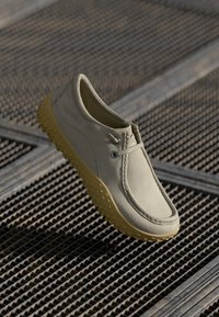 Beige sko med en glatt overdel, rund tå, snøring og gult teksturert gummisåle for grep. Designet for komfort og allsidighet.