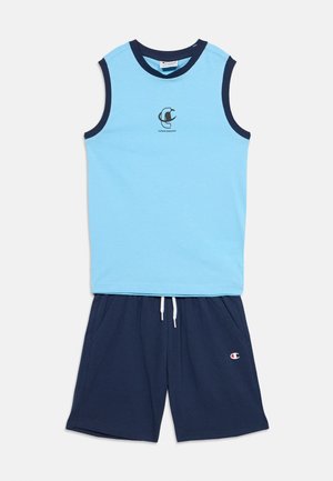 Ærmeløs lyseblå top med mørkeblå kant og logo i midten, kombineret med mørkeblå snøre shorts med sidelommer og lille logo.