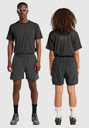 Mann von vorne, der dunkelgraue Sportshorts, ein passendes Shirt, Sonnenbrille, schwarze Socken und Turnschuhe trägt; Frau, die von hinten im gleichen Outfit mit weißen Socken zu sehen ist.