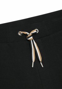 Shorts en coton noir avec une taille à cordon de serrage. Le cordon de serrage présente des rayures brunes, blanches et noires, maintenues par des extrémités en métal argenté.