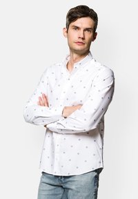 Biała koszula z długim rękawem, z niebieskimi wzorami kwiatowymi i kołnierzykiem, połączona z jasnoniebieskimi dżinsami.