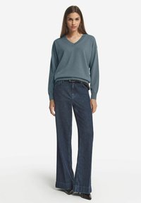 Ljusblå stickad tröja med V-hals, ihopparad med mörka vida jeans. Jeansen har uppvikta nederkant och ett bälte i midjan.