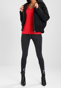 Czarna kurtka puchowa z kapturem, czerwona sweter z dekoltem w serek, ciemnoszare przetarte skinny jeans i czarne botki za kostkę. Gładkie materiały i dopasowany krój.