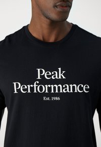 Camiseta de algodón negra con texto blanco: "Peak Performance" y "Est. 1986". Diseño clásico de cuello redondo sin patrones o detalles adicionales.