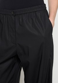 Schwarze, leichte Hose mit elastischem Bund, Knopfverschluss und Seitentaschen, gefertigt aus glattem, strukturiertem Stoff.