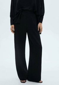 Black wide-leg pants made of textured fabric, featuring a high waist and minimalistic design. Accented with a side tie detail.