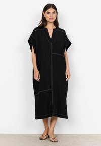 Zwarte kaftan jurk van lichte stof, met een V-hals, korte mouwen en contrasterende witte stiksels over het lichaam.