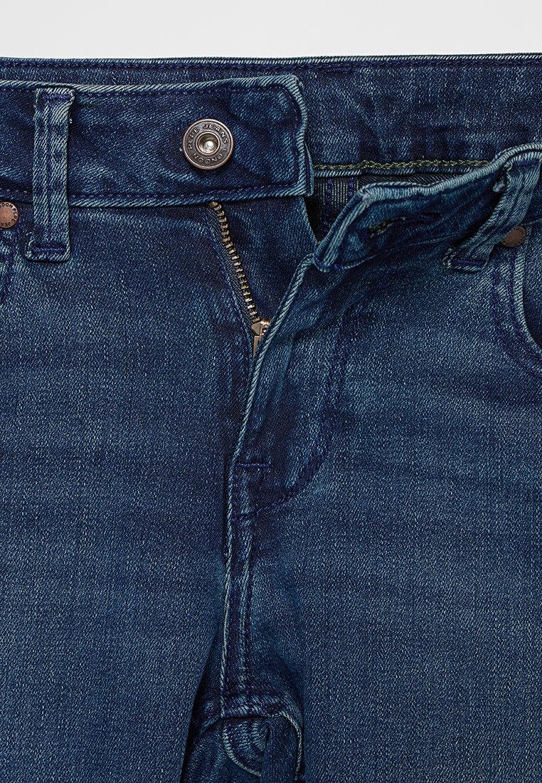 Jeans di denim blu scuro con chiusura a bottone e zip, caratterizzati da un tradizionale design a 5 tasche e una leggera texture sbiadita.