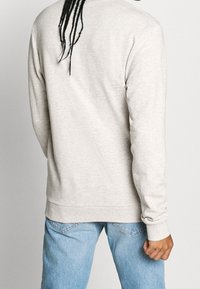 Ljust grå fleecetröja med långa ärmar, rundad halsringning och ribbad fåll, bärs över ljusblå denimjeans. Strukturerad tyg.