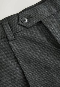 Gray textured fabric of pants with a button closure at the waistband; features a subtle herringbone pattern and clean lines.
