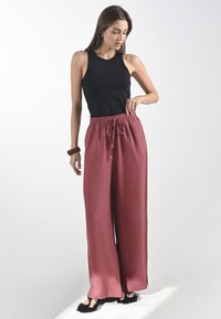 Zwarte tanktop gecombineerd met losse, hoog getailleerde, dieproze broeken met een elastische tailleband en een subtiele textuur. Geaccentueerd met zwarte schoenen.