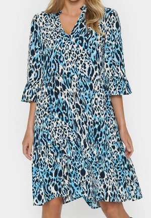 Femme portant une robe mi-longue avec un imprimé léopard bleu, noir et blanc, manches trois-quarts et col en V.